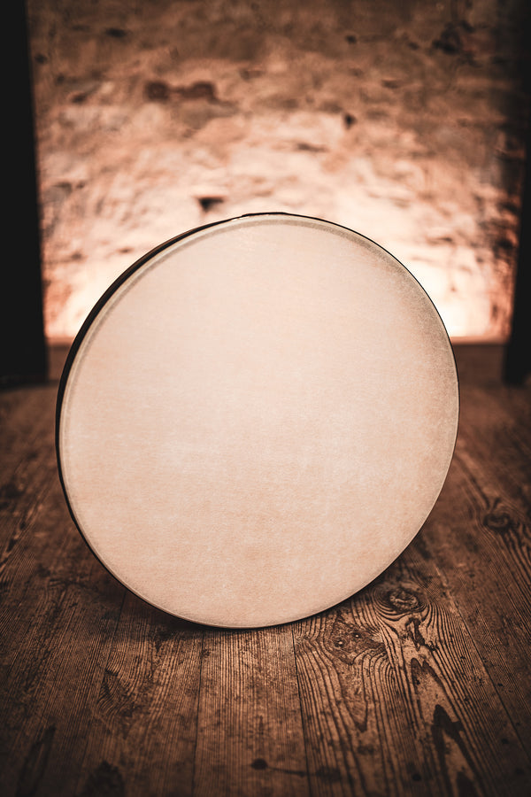 An 18" Woven Synthetic Head Hand Drum by Meinl, known for its exceptional acoustic properties, placed on a round table made of wood and situated in front of a cozy fireplace.