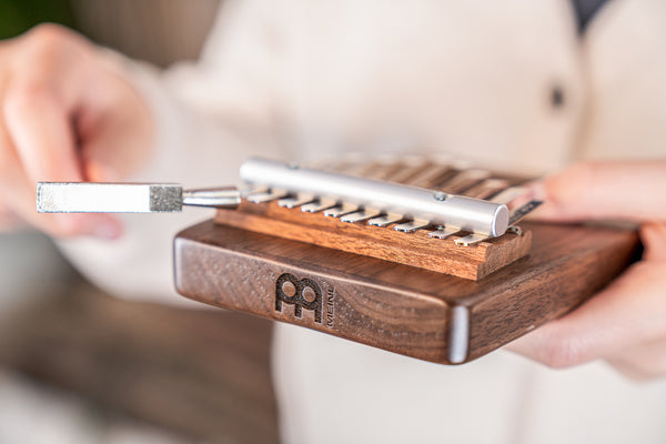 A musician is holding a Meinl 10 notes Kalimba, Tree Of Life, Black Walnut, creating soothing sounds for sound healing therapy.