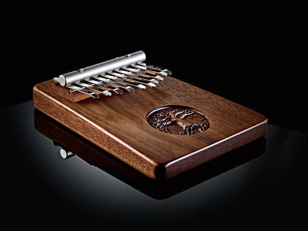 A Meinl 10 notes Kalimba, Tree Of Life, Black Walnut, a wooden musical instrument, on a black surface.