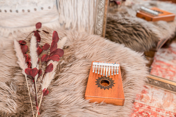 A Meinl Mahogany 10 notes Kalimba sits on a furry rug next to a mirror, creating a serene atmosphere for meditation or sound healing therapy.