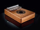 A Meinl 10 notes Kalimba, made of Mahogany, is a wooden musical instrument used for sound healing therapy and meditation, resting on a sleek black surface beneficial for yoga practices.