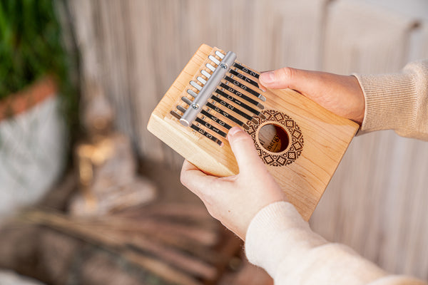 A person is holding a Maple Thumb Piano, also known as a Sonic Energy Soundhole Kalimba, a wooden musical instrument used for sound healing therapy.