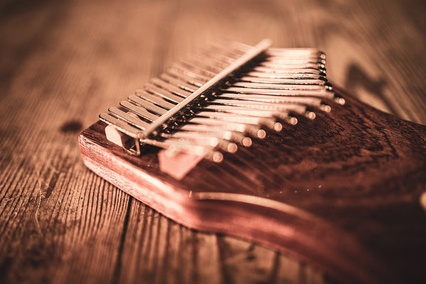 A Meinl 17 notes Kalimba, Sapele melodic instrument, resembling a wooden hammer dulcimer, placed elegantly on a wooden table.