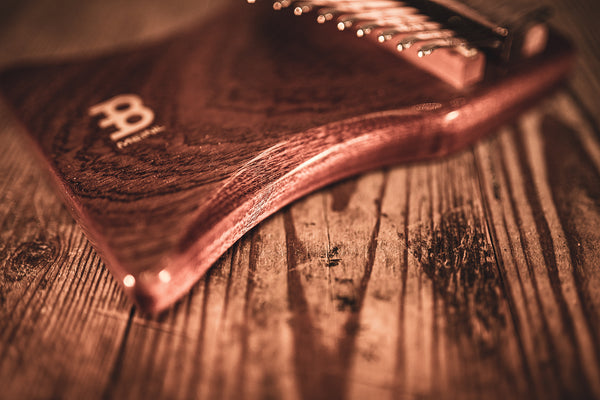 A Meinl 17 notes Kalimba, Sapele, a melodic instrument made of wood, is sitting on top of a wooden table.