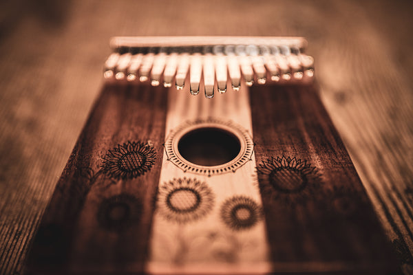 The Meinl 17 notes Kalimba, Maple & Acacia is a melodic instrument made of wood, producing enchanting sounds in the C Major scale. It is placed on a wooden table for display.