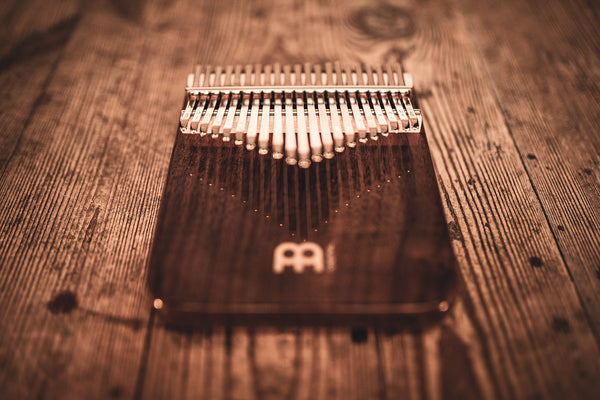 A melodic instrument, the Meinl 21 notes Kalimba, Black Walnut, is placed on a wooden table made of black walnut wood.