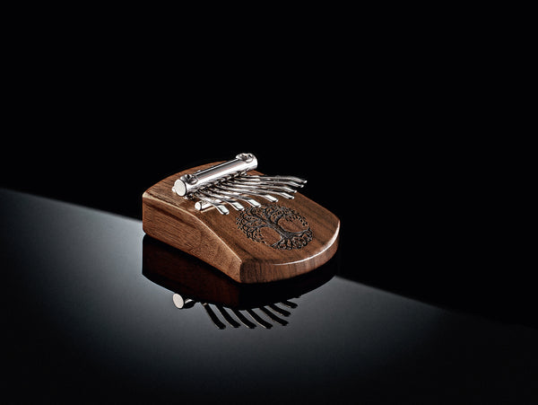 An 8 notes Kalimba by Meinl, an 8 notes kalimba made of Black Walnut wood and featuring a Tree Of Life design, popular among musicians and used for sound healing therapy, is sitting on top of a black surface.