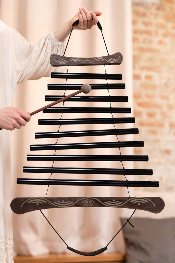 A woman is holding a Meinl Meditation Flow Chime 38" / 95 cm, 432 Hz, 10 Notes, C Minor, Black xylophone, providing a calming sound therapy experience for relaxation.