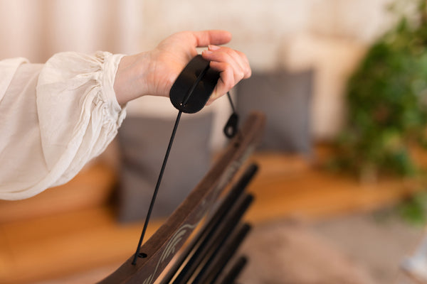 A person holding a Meinl Meditation Flow Chime 38" / 95 cm, 432 Hz, 10 Notes, C Minor, Black remote control on a wooden chair, engaging in relaxation and sound therapy for meditation.