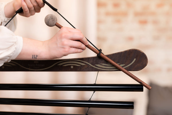 A woman is holding a Meinl Meditation Flow Chime 38" / 95 cm, 432 Hz, 10 Notes, E Minor, Black, creating a soothing sound for relaxation and sound therapy.