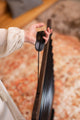 A woman is holding a Meinl Meditation Flow Chime 38" / 95 cm, 432 Hz, 10 Notes, E Minor, Black on a rug, creating a tranquil atmosphere for relaxation with the soothing sound therapy it offers.