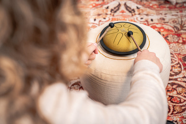A girl, who is a sound therapy practitioner, playing a Meinl 6" Tongue Drum in B Major and Gold on a rug with pre-tuned notes.