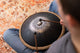 A man creating meditative sound on a Meinl 16" Tongue Drum, D Kurd, Lasered floral design, Black, using high-quality stainless steel.