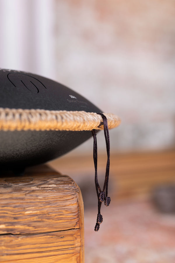 A high-quality Meinl 16" Tongue Drum, D Kurd, Lasered floral design, Black sitting on top of a wooden table, emitting a meditative sound.