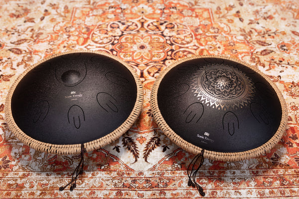 Two high-quality Meinl 16" Tongue Drums, D Kurd, Lasered floral design, Black sitting on a rug, producing a meditative sound.