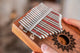 A person holding a Meinl 17 notes Kalimba, Mahogany, in front of a fireplace for sound healing therapy.