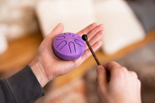 A person holding a compact size Meinl 3" Tongue Drum, A Major, Lotus Flower, Purple in their hand.