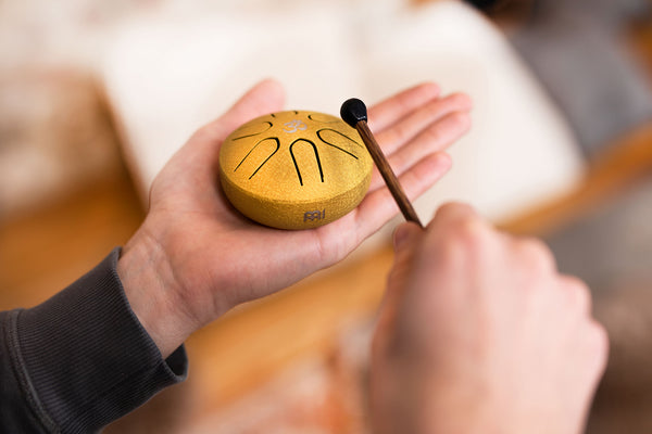 A sound therapist is holding a Meinl 3" Tongue Drum, A Major, OM, Gold, a small yellow object, in their hand.